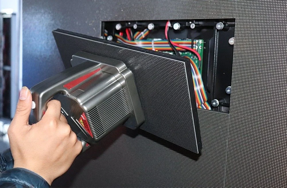Technician lifting a front-service LED module out of an installed indoor LED display with a suction tool to expose the internal data and power wiring