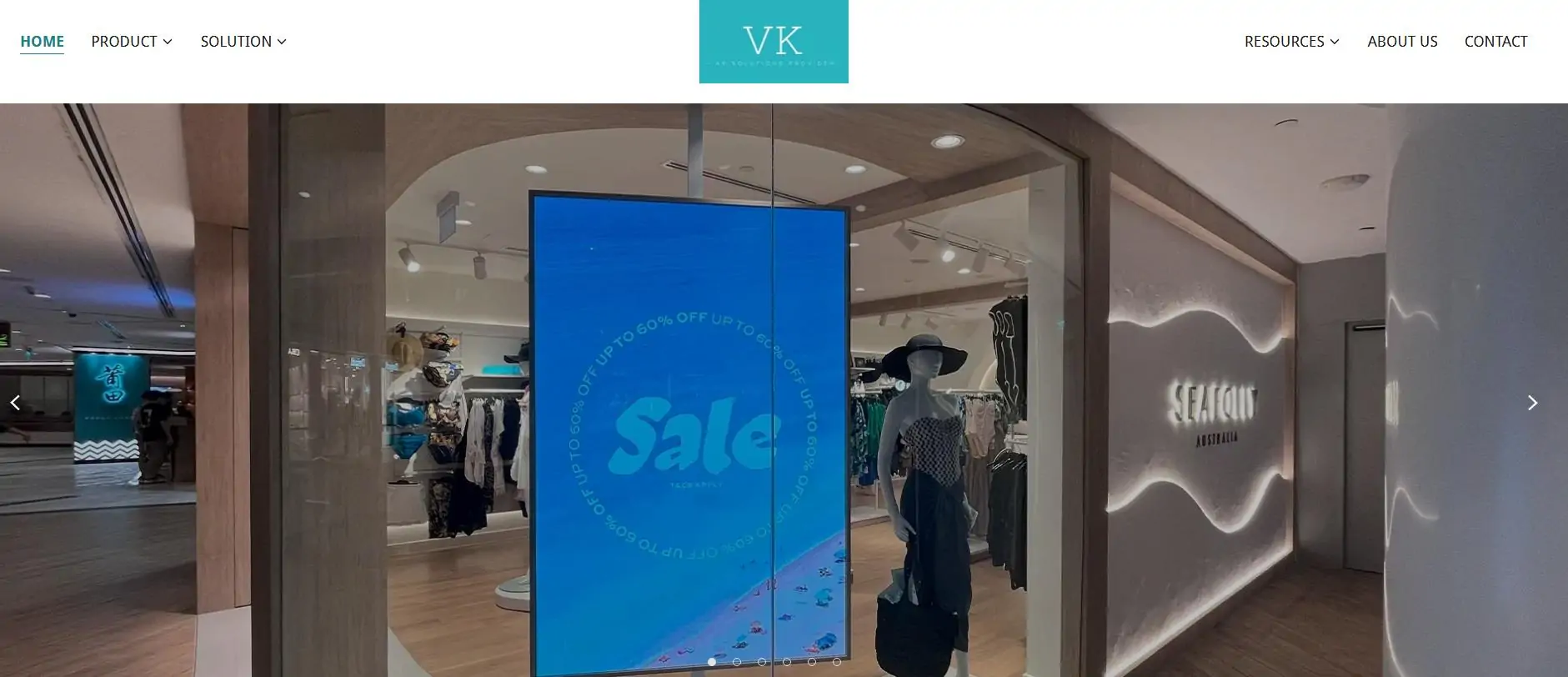 Clothing store display in a shopping mall with a tall blue Sale screen and a mannequin near the entrance.