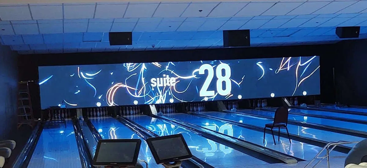 Wide indoor LED display above bowling lanes showing graphics against dark surroundings